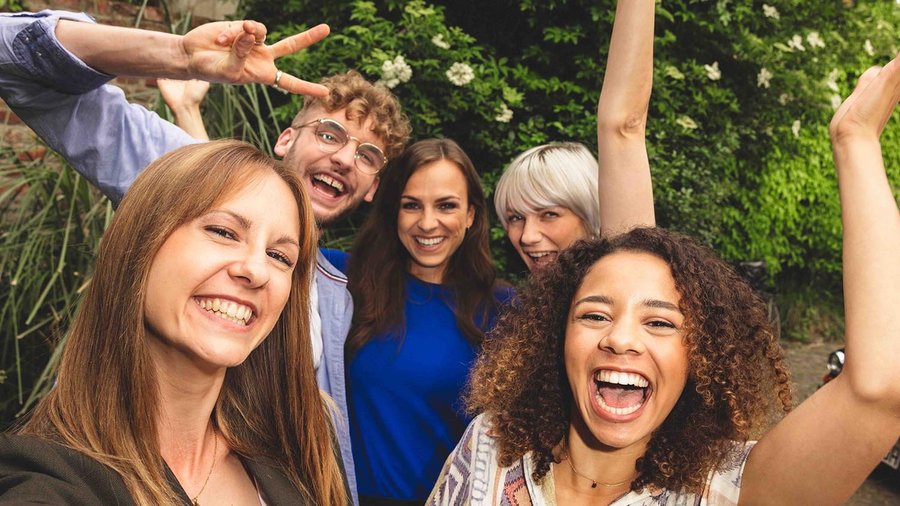 Planowanie wakacji z przyjaciółmi - jak to działa? Pięciu przyjaciół stojących blisko siebie i śmiejących się do kamery