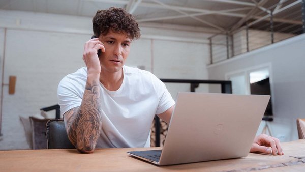 Powodzie i samochody – które ubezpieczenie pokrywa koszty? Młody mężczyzna siedzący przed laptopem i rozmawiający przez telefon