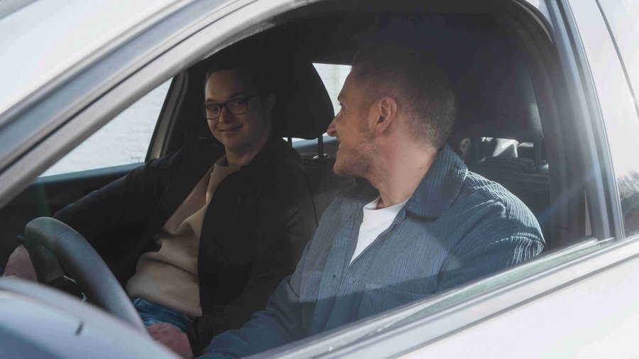 Czy posiadanie auta ma sens? Dwóch młodych mężczyzn siedzących w samochodzie i uśmiechających się do siebie
