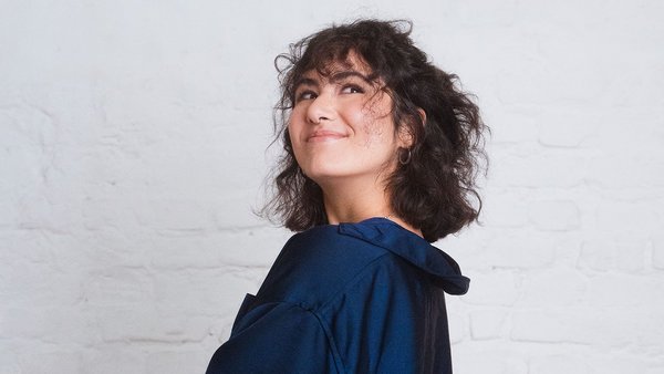 Czy zasada 50-30-20 działa również wtedy, gdy niewiele zarabiasz? Kobieta w niebieskiej koszuli i brązowych włosach spogląda psotnie.