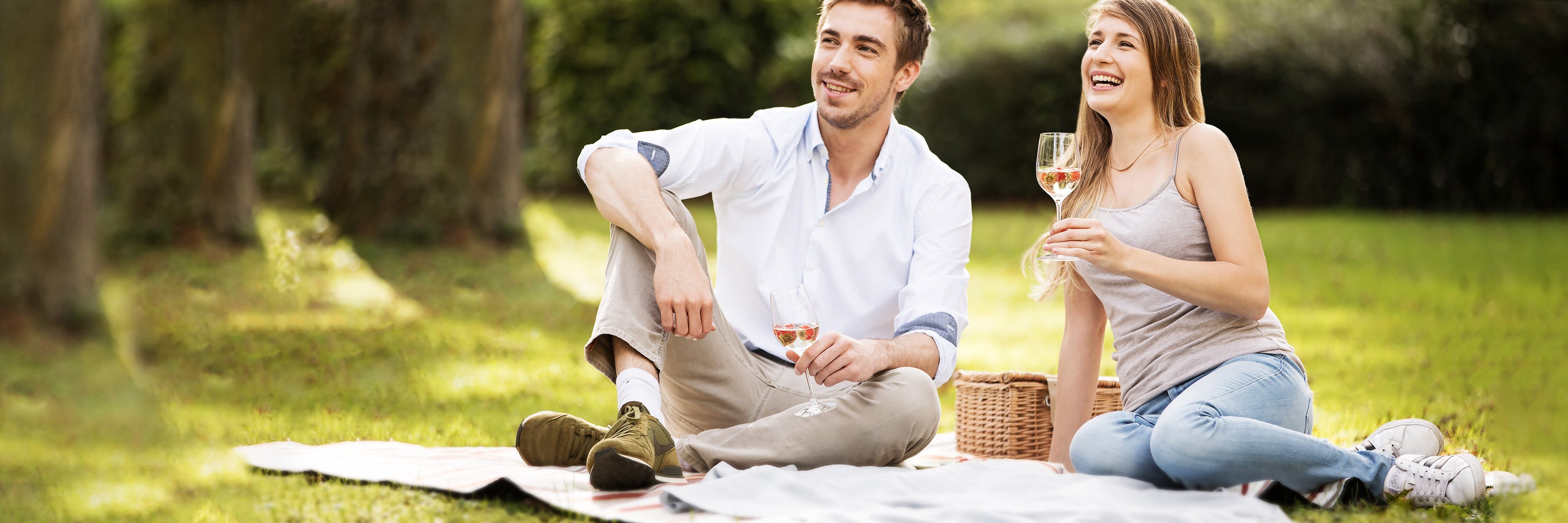 Para siedząca na kocu w parku pije szampana i uśmiecha się. Para siedząca na kocu w parku pije szampana i uśmiecha się.
