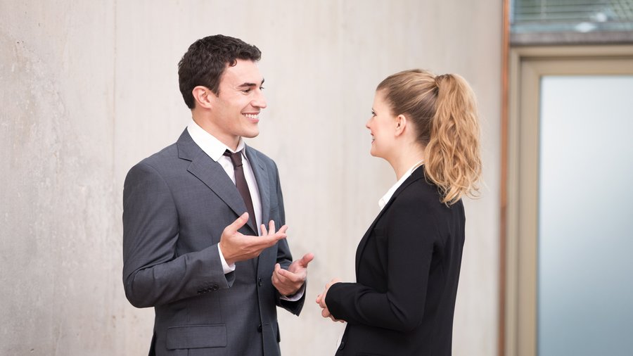Pełna zaufania i ścisła współpraca wiąże nas z naszymi Partnerami. Mężczyzna i kobieta w strojach biznesowych prowadzą ożywioną rozmowę na korytarzu.